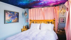 Een slaapkamer met een bed, een nachtkastje, een wandlamp en een plafond met een sterrenstelsel motief.