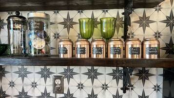 A kitchen shelf with coffee pods and spice jars labeled with names like "Earl Grey" and "Smoothing Peppermint."