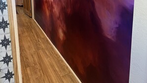 Een gang met een groot abstract schilderij op de muur, houten vloeren en een deur met een gordijn met stermotief.