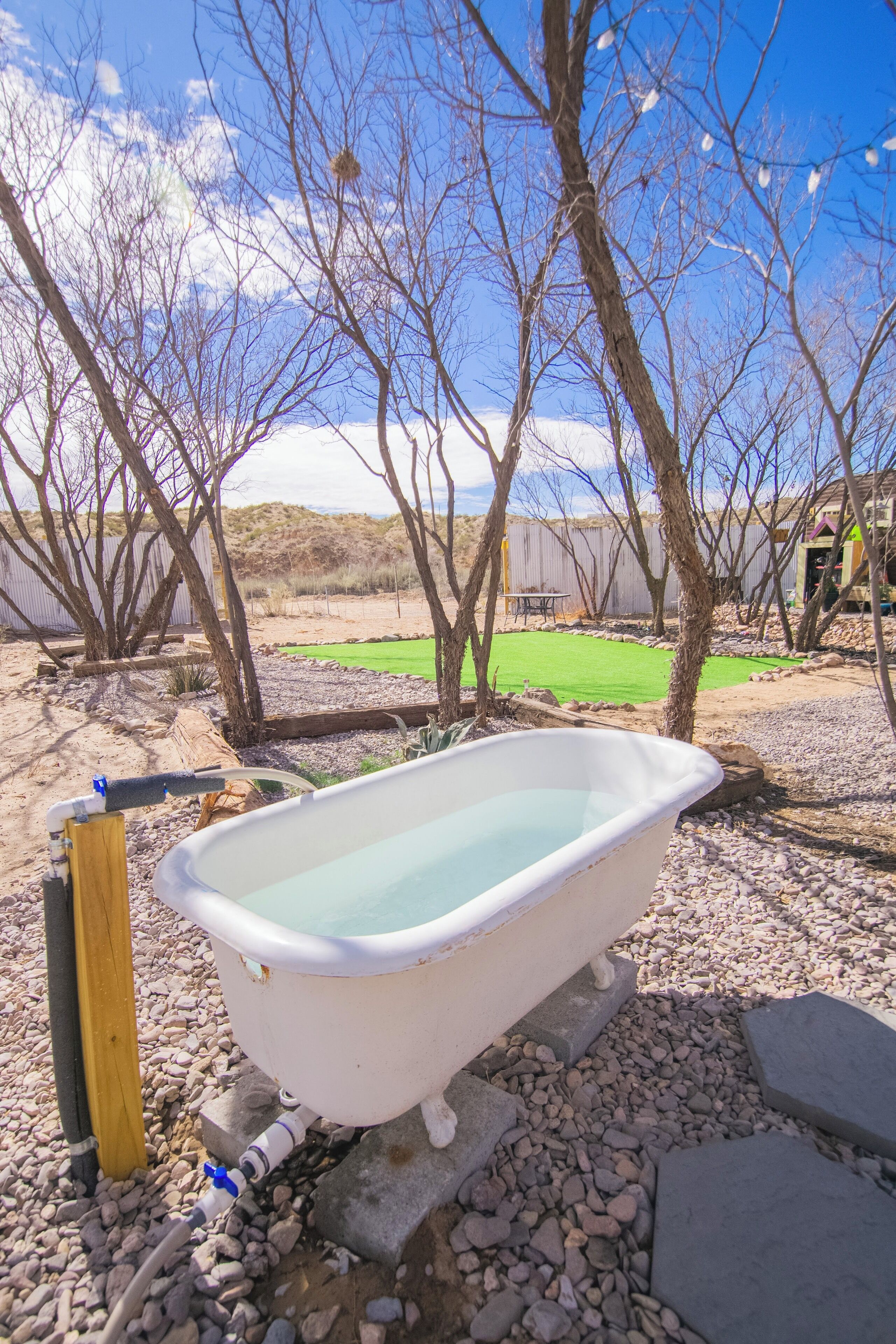 Eine weiße Badewanne in einer Außenanlage mit blauem Himmel und Bäumen im Hintergrund.