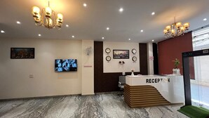 A reception area with a marble floor, a reception desk labeled "RECEPTION," a television mounted on the wall, and a chandelier. - Ivory Airport (New Delhi)