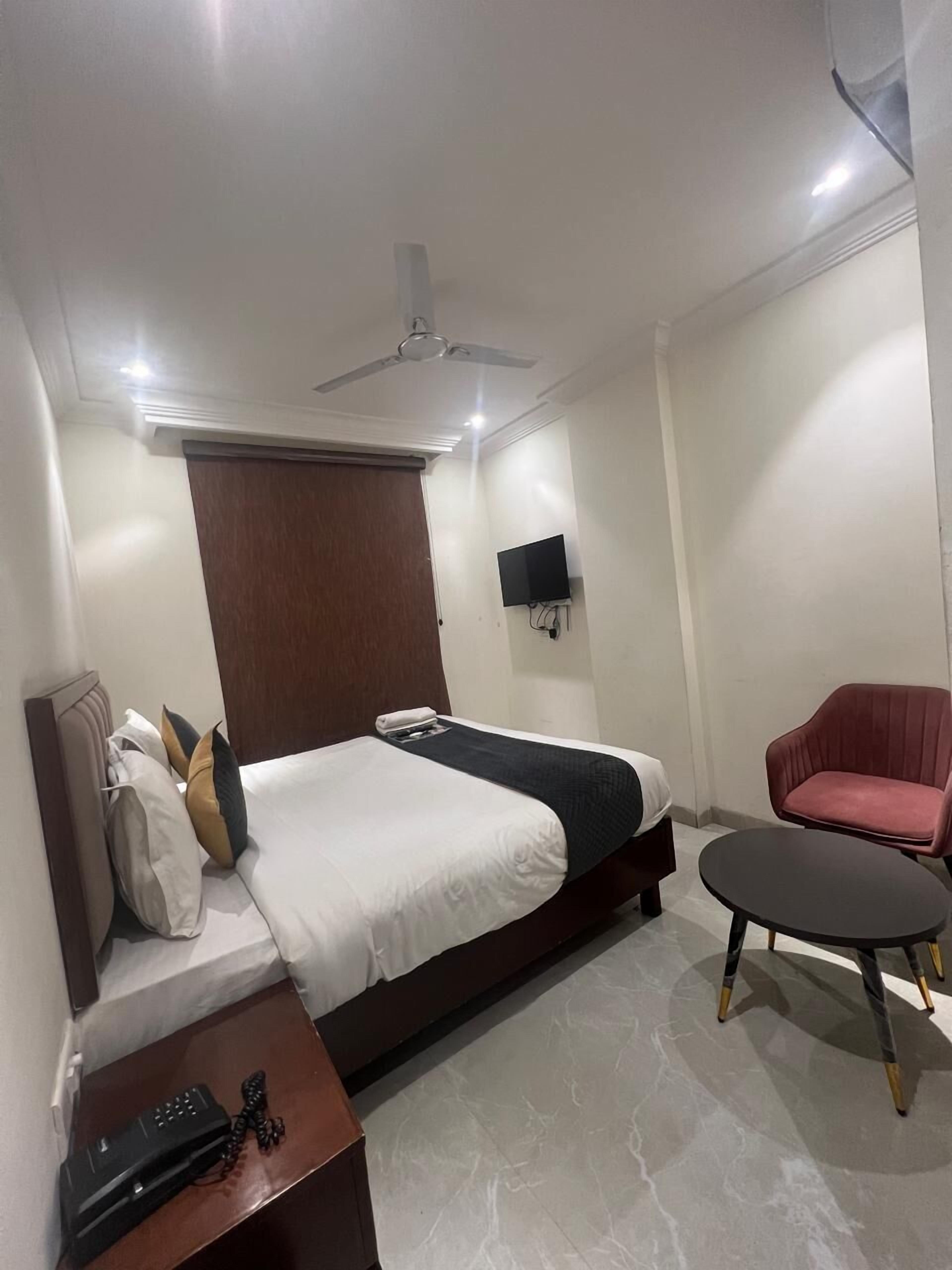 A hotel room with a bed, a desk with a telephone, a chair, a television mounted on the wall, and a ceiling fan.