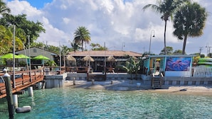 Zona costera con agua cristalina, un muelle de madera y un restaurante con terraza.