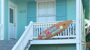A turquoise house with a white porch, a surfboard sign, and a staircase leading to the entrance. - Surf House Galveston (Galveston)