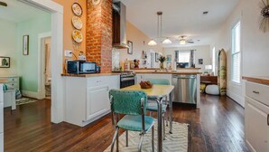 A kitchen with a brick wall, stainless steel appliances, and a dining area with teal chairs. - Surf House Galveston (Galveston)