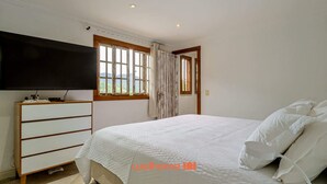 A bedroom with a bed, a TV, a dresser, and a window with curtains. - Casa Confortável em Angra do Reis Proximo a Praia (Angra dos Reis)