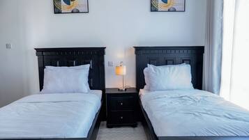 Ein Hotelzimmer mit zwei Betten, einem Nachttisch mit Lampe und zwei abstrakten Bildern an der Wand.