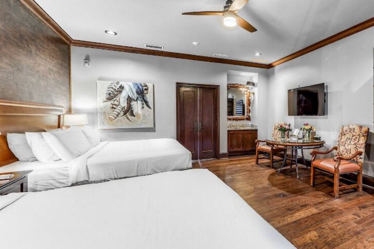 A hotel room with a large bed, a desk with a chair, a dining table with chairs, and a TV mounted on the wall.