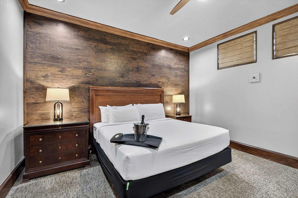 A neatly made bed with a wooden headboard, two bedside lamps, a nightstand, and a wooden accent wall.