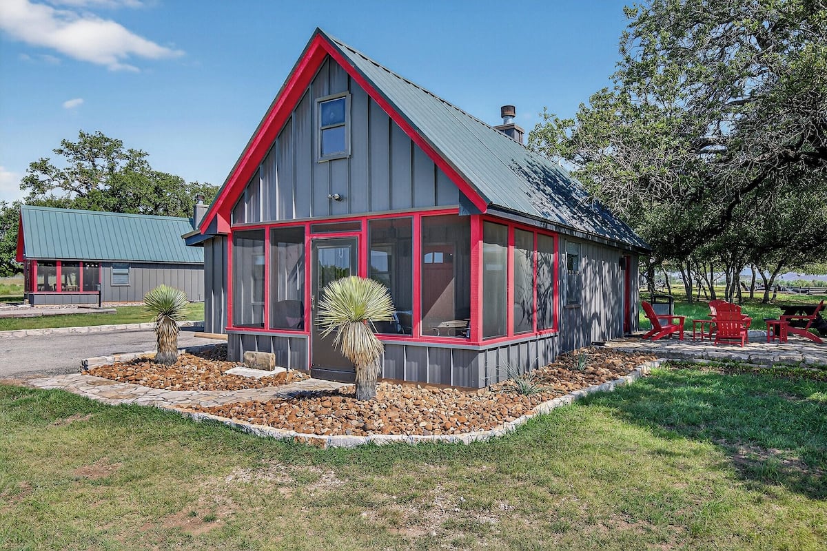 A two-story building with a red-framed glass enclosure, a stone foundation, and a landscaped garden with a yucca plant.