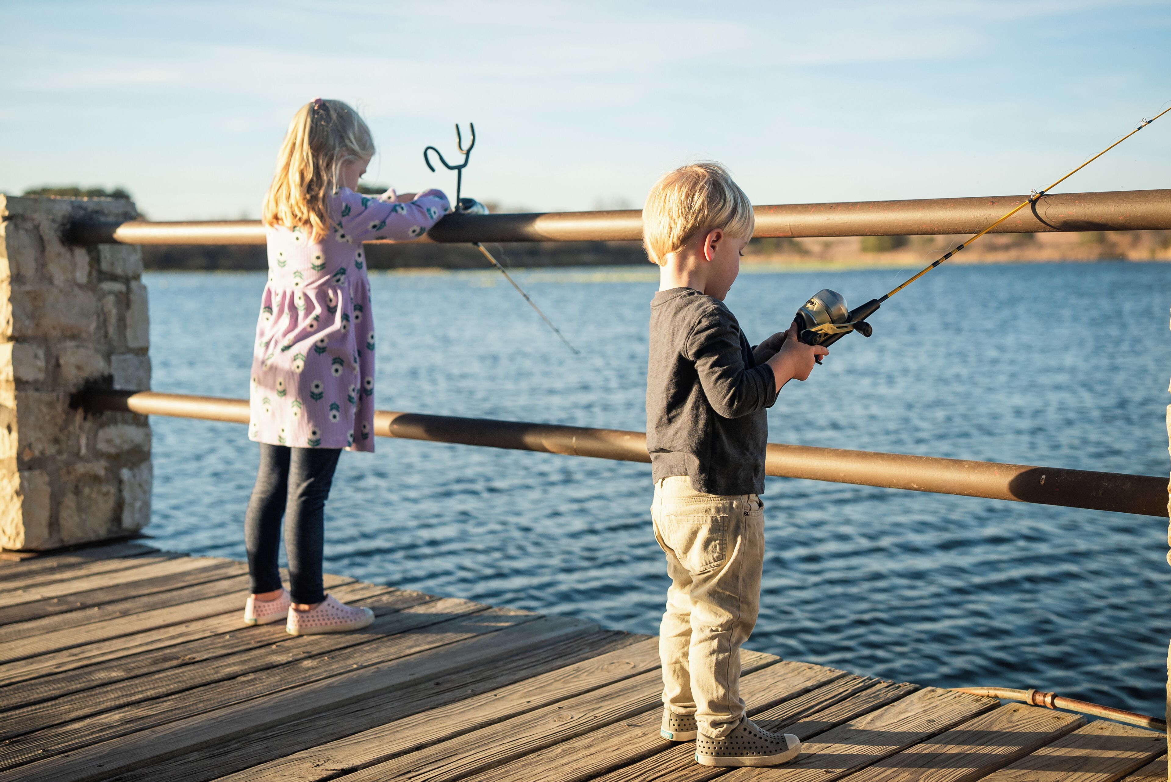 Two children fishing on a wooden pier with a view of the water.