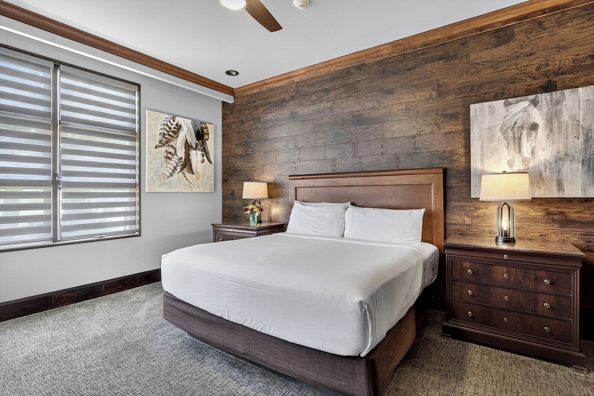 A bedroom with a large bed, wooden headboard, two bedside tables with lamps, and artwork on the walls.