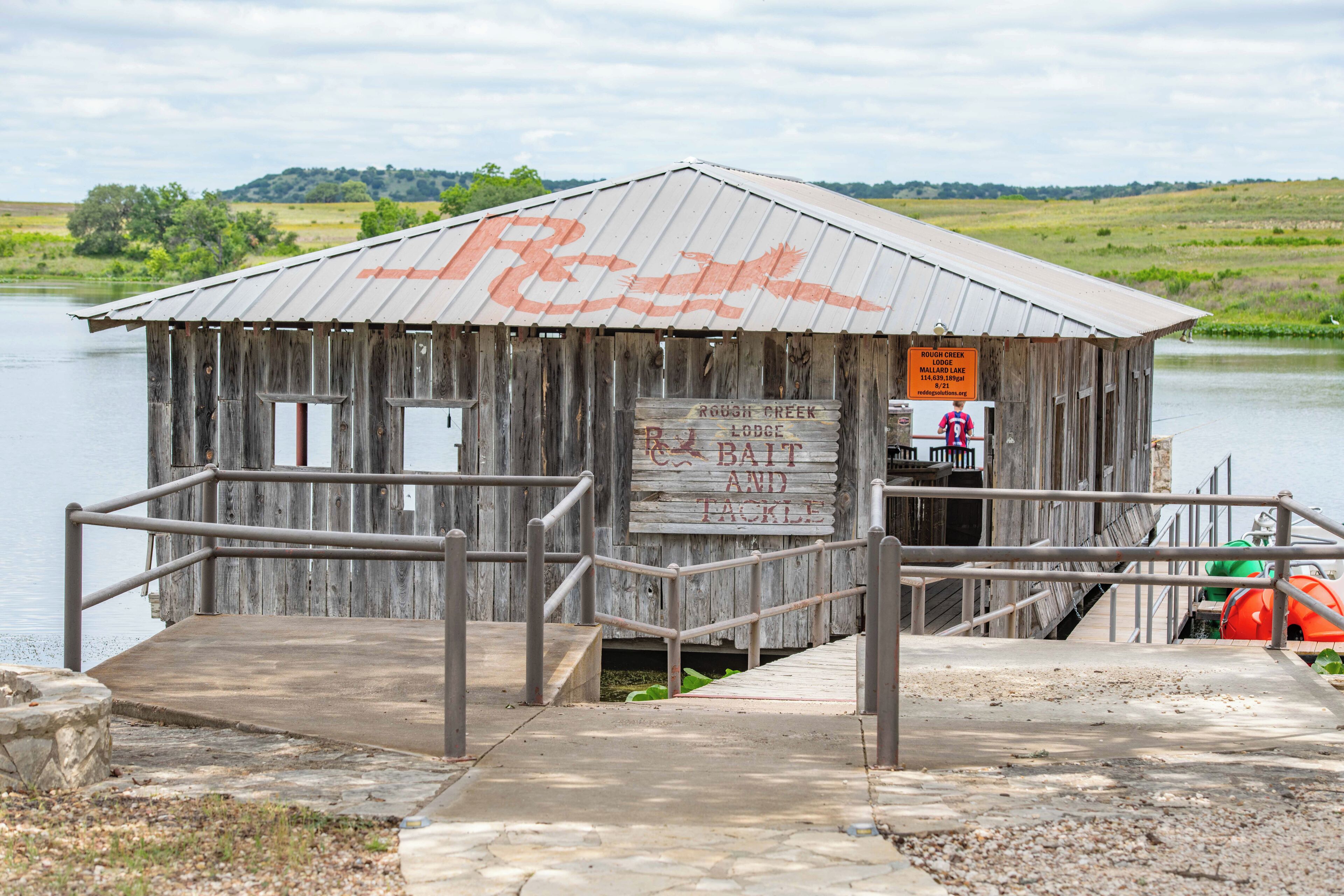 A rustic wooden cabin with a metal roof, a sign indicating it is a Rough Creek Lodge, and a dock extending into a body of water.