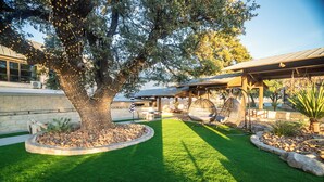 A landscaped garden with a large tree, a covered seating area, and a patio with outdoor furniture. - Rough Creek Lodge Ranch and Resort (Glen Rose)