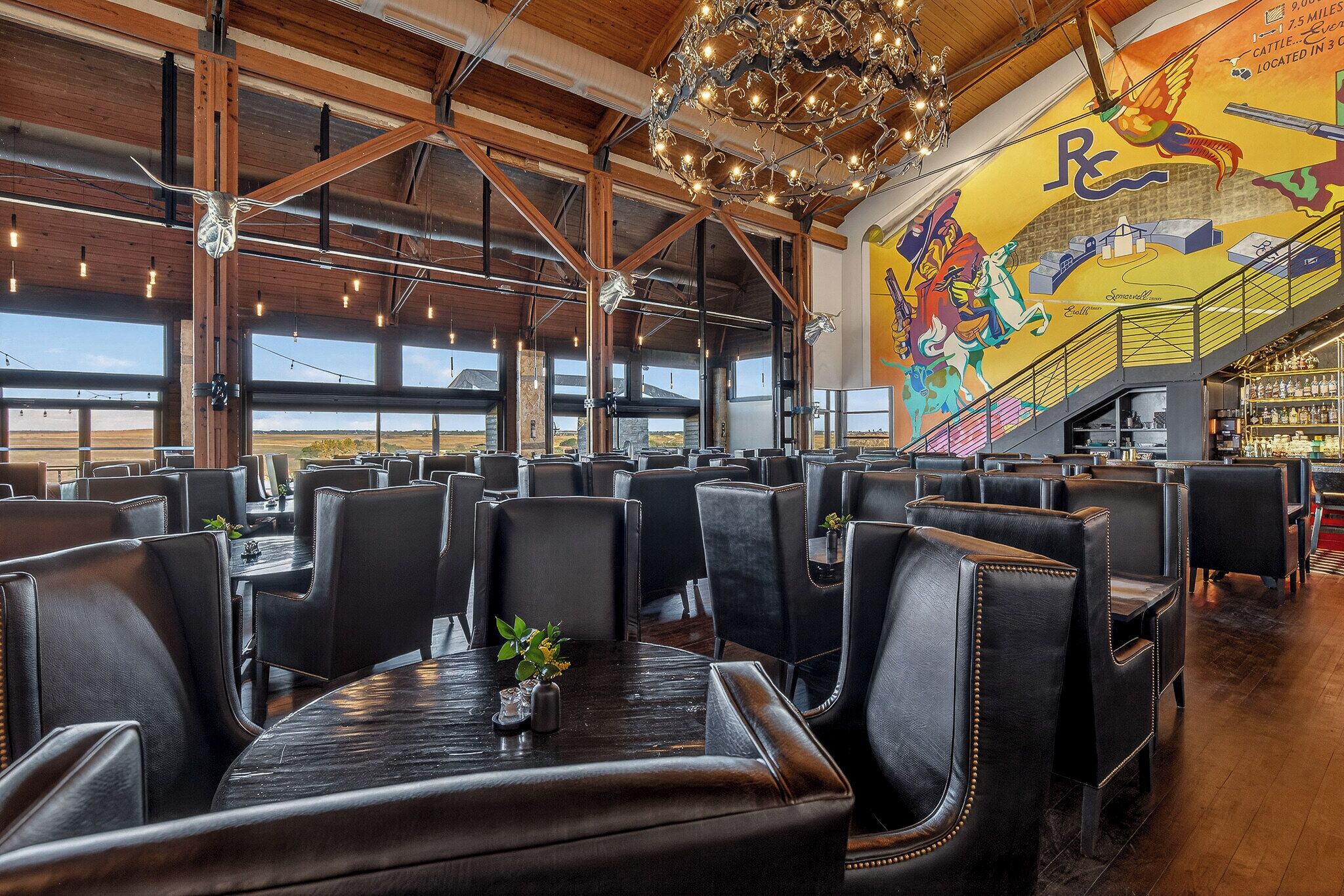 A spacious dining area with leather booths, a chandelier, and a mural on the wall.