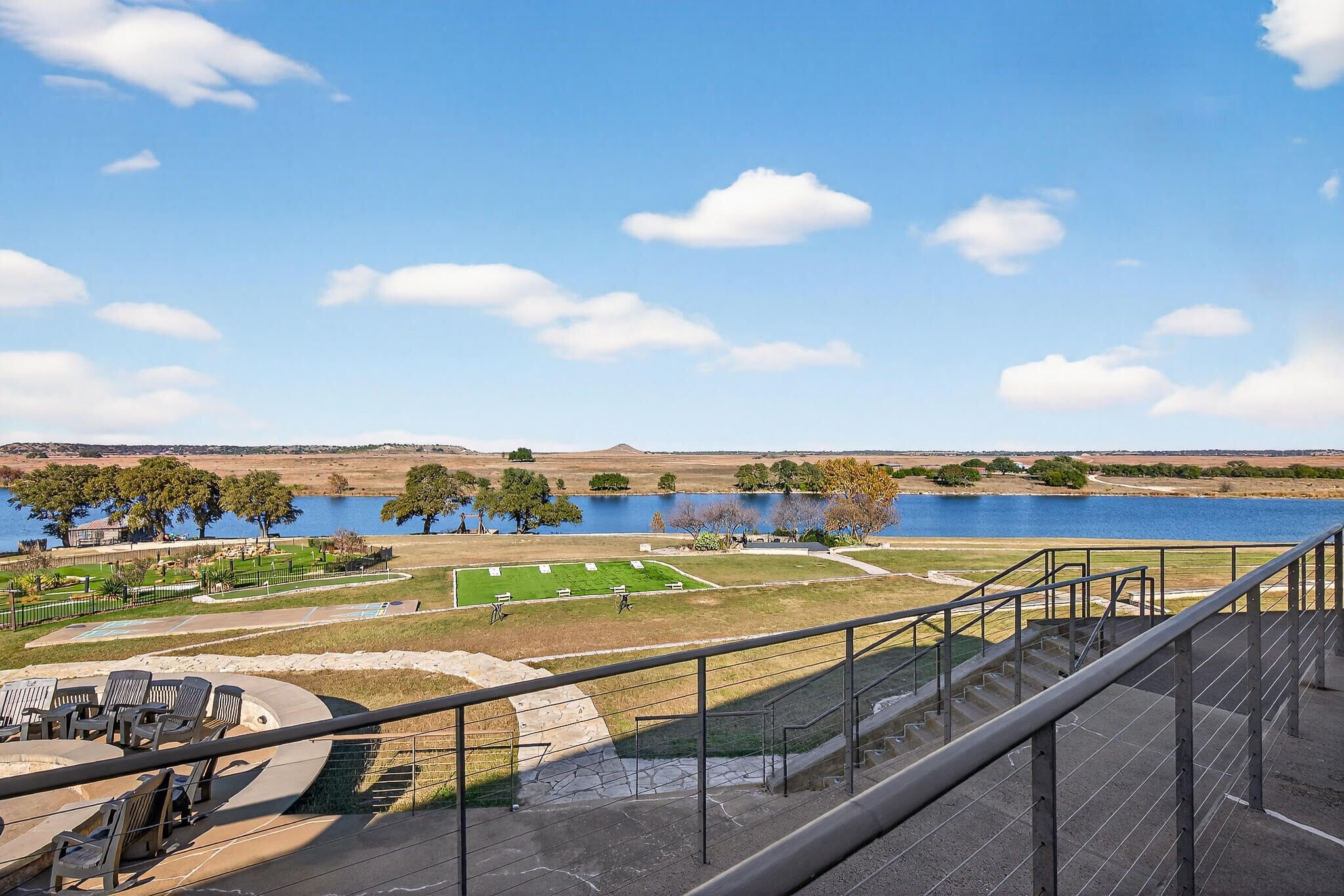 A view from a balcony overlooking a park with a lake, a tennis court, and a grassy area.