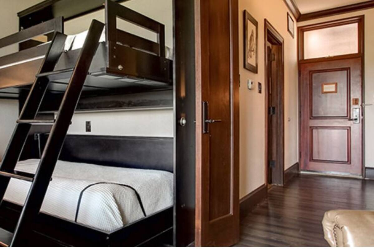 A bunk bed room with a desk, a lamp, and a door leading to another room.