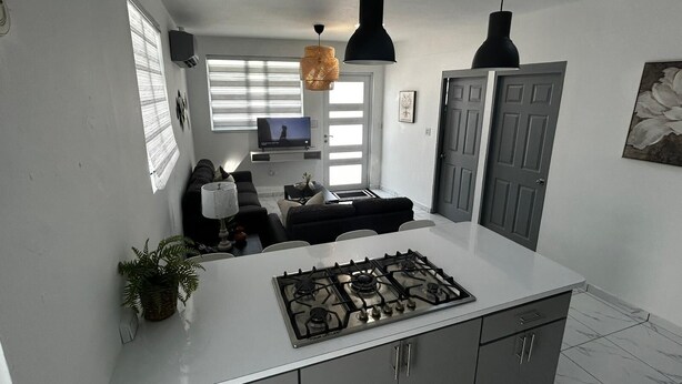 Een moderne keuken met een gasfornuis, een eethoek met tafel en stoelen, en een zithoek met bank en televisie.