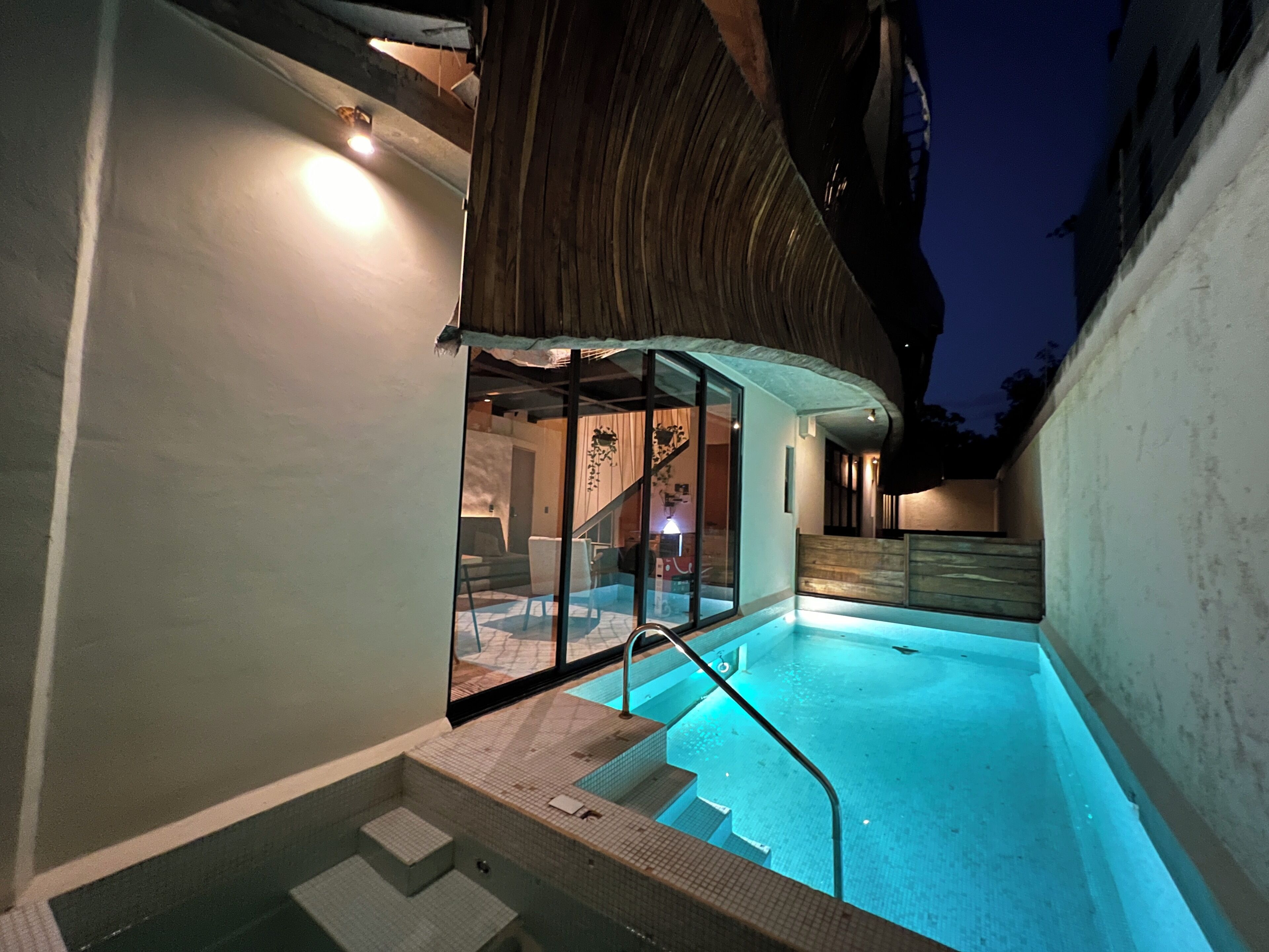A modern outdoor swimming pool with glass walls, steps leading into the pool, and a wooden ceiling structure.