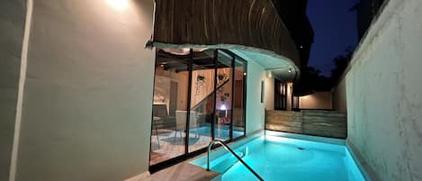 A modern outdoor swimming pool with glass walls, steps leading into the pool, and a wooden ceiling structure.
