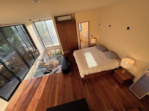 A bedroom with a large bed, wooden flooring, a sliding glass door leading to a balcony, and a small bedside table with a lamp. - Super Loft House Style with Private Pool and Garden (Tulum)
