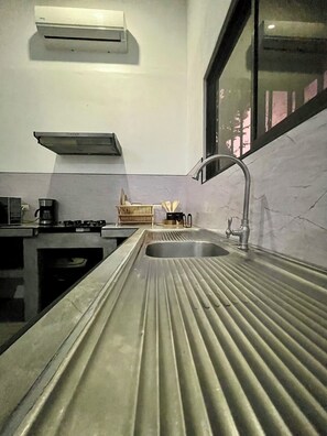A modern kitchen with a stainless steel countertop, a built-in sink, a gas stove, and a window overlooking a cityscape.