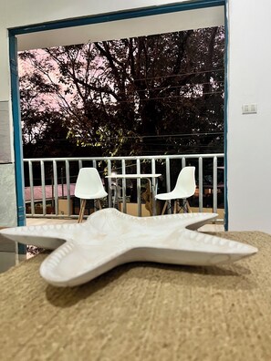 A room with a starfish-shaped object on a textured surface, a white chair, and a balcony with a railing and trees in the background.