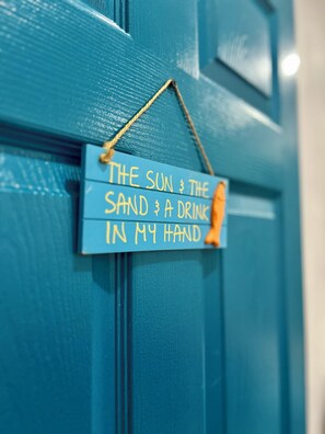 A blue door with a wooden sign that reads "The sun, the sand, a drink in my hand."