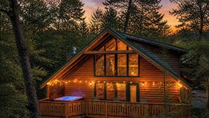 Een houten chalet met een jacuzzi op het terras, omgeven door bomen.