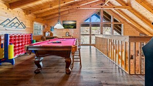 Een houten interieur met een pooltafel, een biljarthouder en een groot raam dat uitzicht biedt op de omgeving.