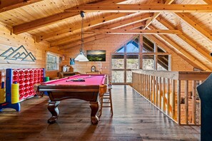 A wooden interior with a pool table, a billiards rack, and a large window providing a view of the outdoors. - Beautiful 2-bedroom cabin, minutes to downtown Gatlinburg! (Gatlinburg)