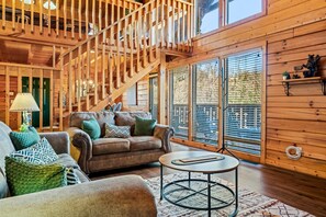 L’intérieur d’un chalet chaleureux, avec un escalier en bois, un canapé en cuir et une table basse ronde.