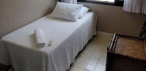 Ein Einzelbett mit weißer Bettwäsche, einer Fernbedienung und einem gerollten Handtuch.
