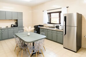 A compact kitchen with grey cabinets, a stainless steel refrigerator, and a dining table with chairs. - Pousada Casarão (Campo Alegre)