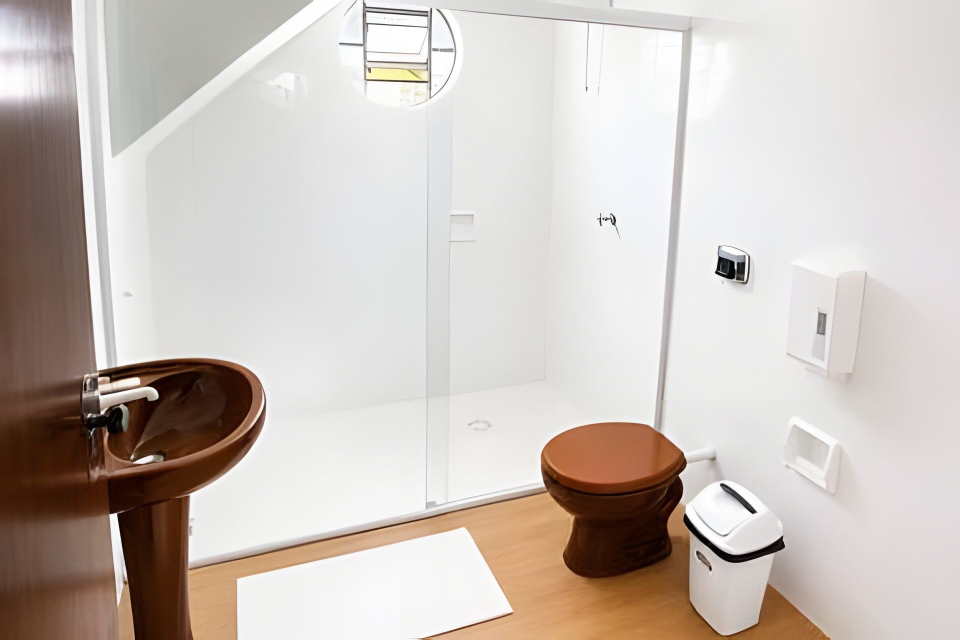 A bathroom with a glass shower enclosure, a toilet, a sink, and a trash bin.