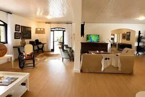 A spacious living room with a large television, a fireplace, and a dining area with a table and chairs. - Pousada Casarão (Campo Alegre)