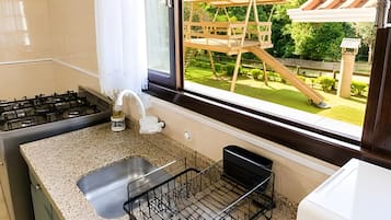 A kitchen with a granite countertop, a stainless steel sink, and a window overlooking a wooden deck with a slide.