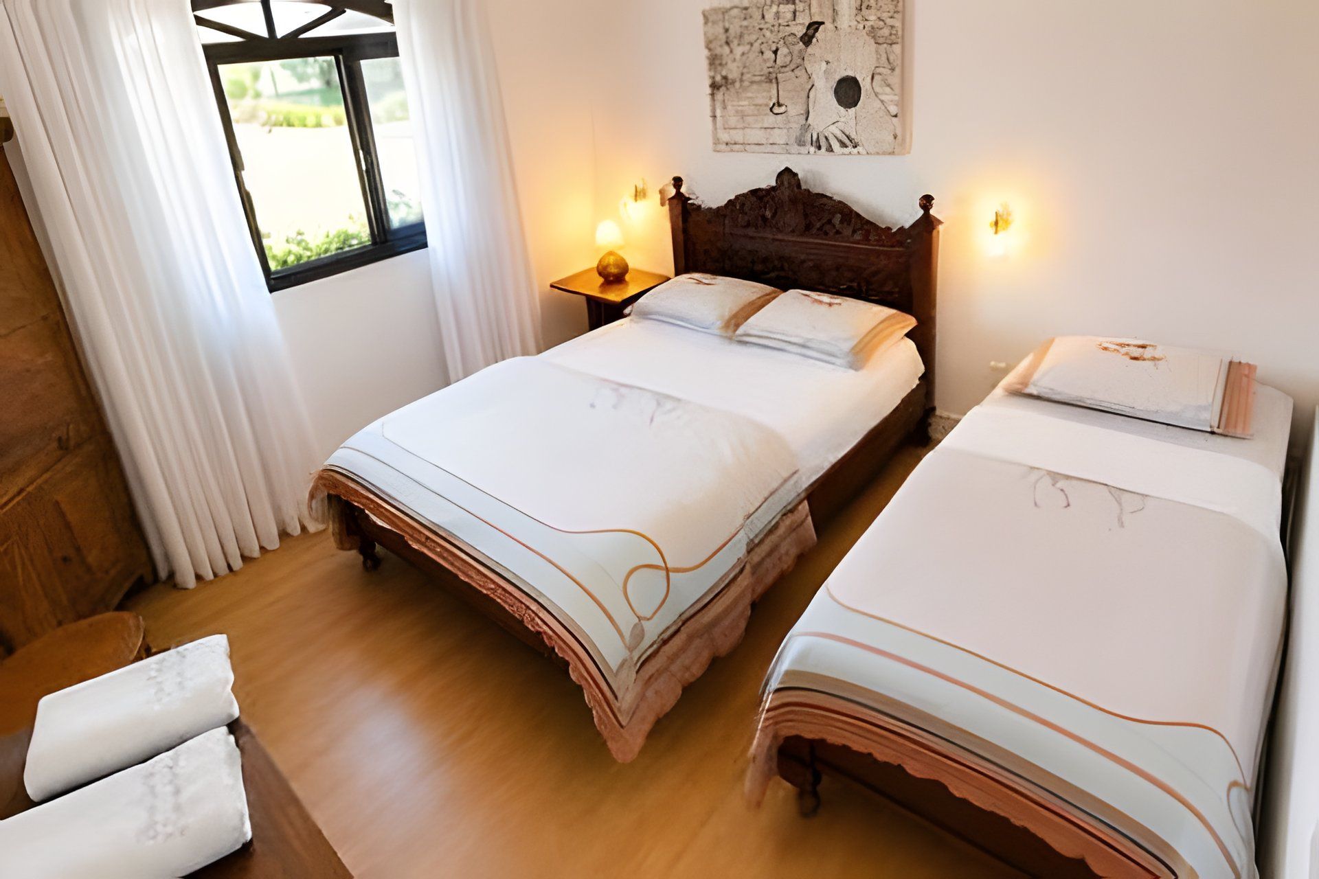 A double bed with a wooden headboard, a bedside table with a lamp, and a window with curtains.