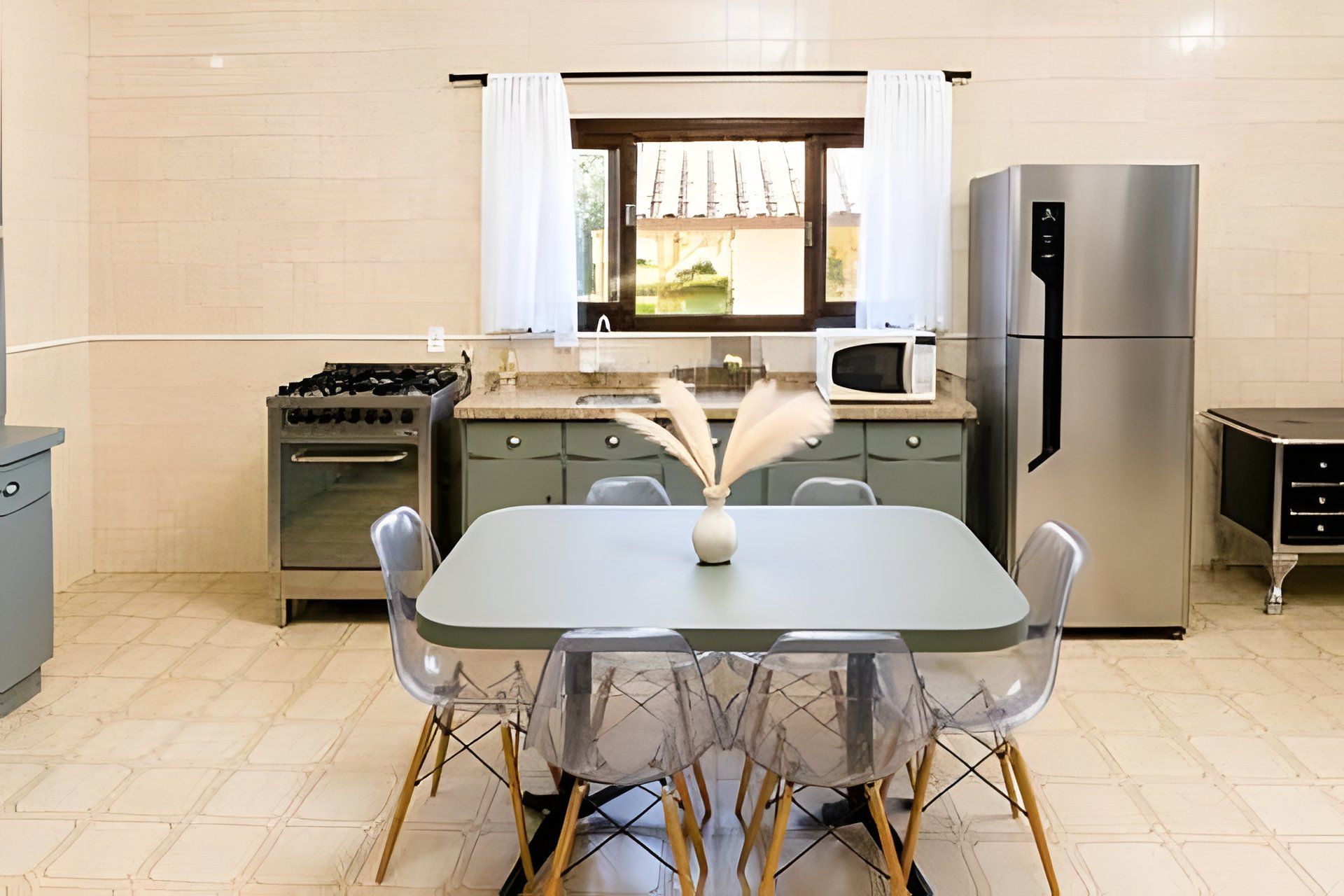 Moderni keittiö, jossa on ruokapöytä, tuolit, jääkaappi, liesi ja mikroaaltouuni.