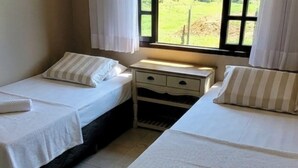 Een kamer met twee eenpersoonsbedden, een nachtkastje met lades, een raam met gordijnen en uitzicht op de omgeving.