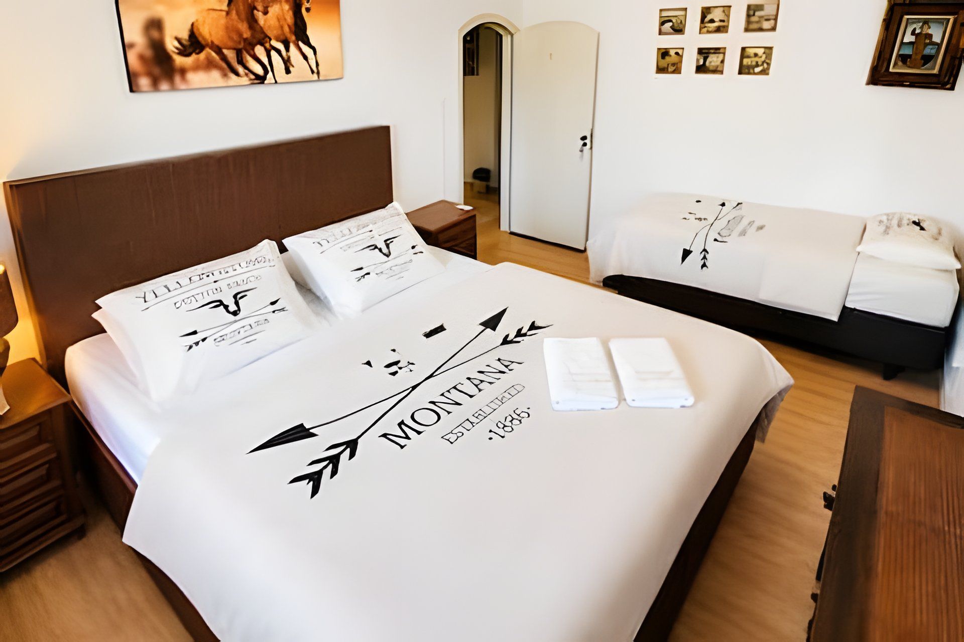 Una cama bien tendida con una colcha blanca que muestra un logotipo y el nombre 'MONTANA' junto con el año de fundación '1835'.