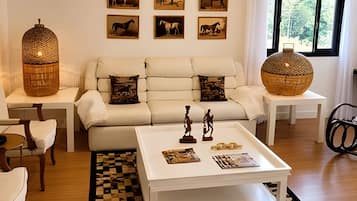 A modern living room with a white sofa, a coffee table with decorative items, and framed horse paintings on the wall.