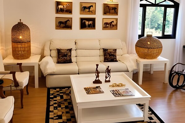 A modern living room with a white sofa, a coffee table with decorative items, and framed horse paintings on the wall. - Pousada Casarão (Campo Alegre)