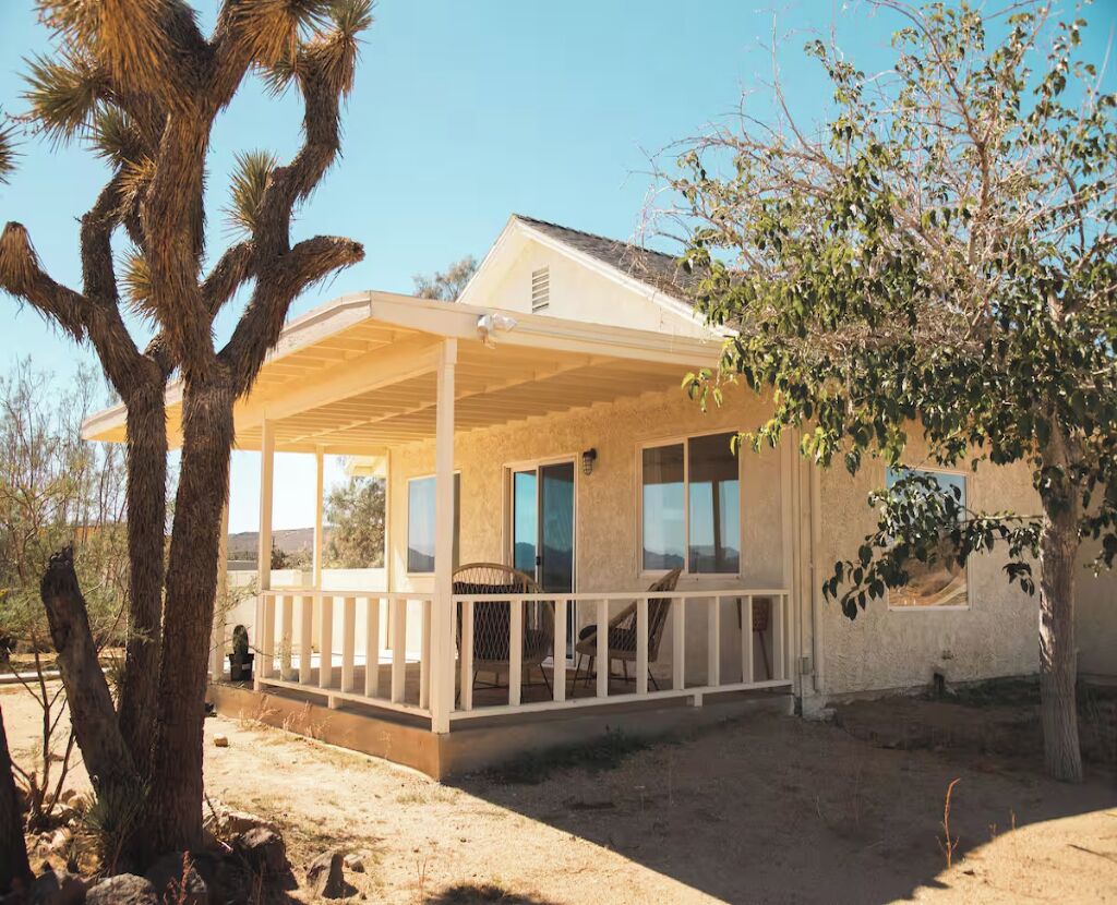 A single-story house with a covered porch, large windows, and a desert landscape.