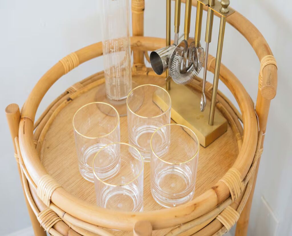 A wicker chair with a tray holding four clear glasses and a metal object.