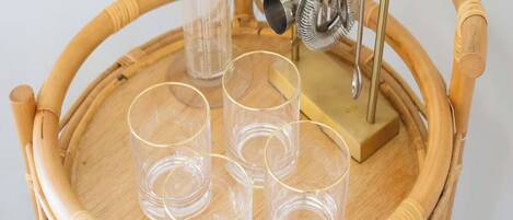 A wicker chair with a tray holding four clear glasses and a metal object.