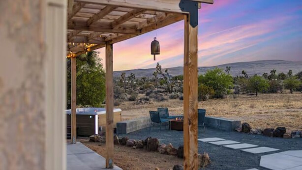 Eine hölzerne Pergola mit Feuerstelle und Sitzbereich, mit Blick auf eine Wüstenlandschaft und einem klaren Himmel.