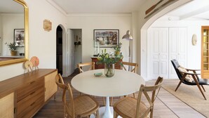 Un comedor con una mesa redonda, sillas de mimbre, un armario de madera y un espejo grande.