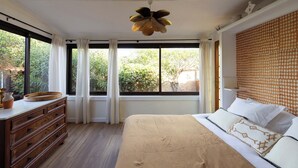 Un dormitorio con una cama grande, un aparador de madera, un ventilador de techo y una ventana con cortinas.