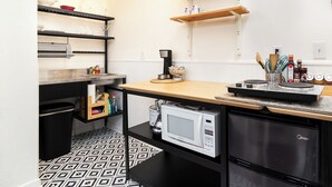 Een praktische keuken met vloer in zwart-wit patroon, een magnetron, een koelkast en houten planken met keukengerei.